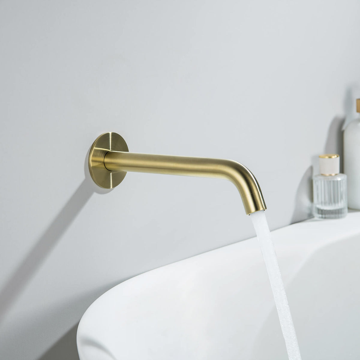 Aquavit Circular brushed gold wall-mounted bath spout delivering water into a bathtub