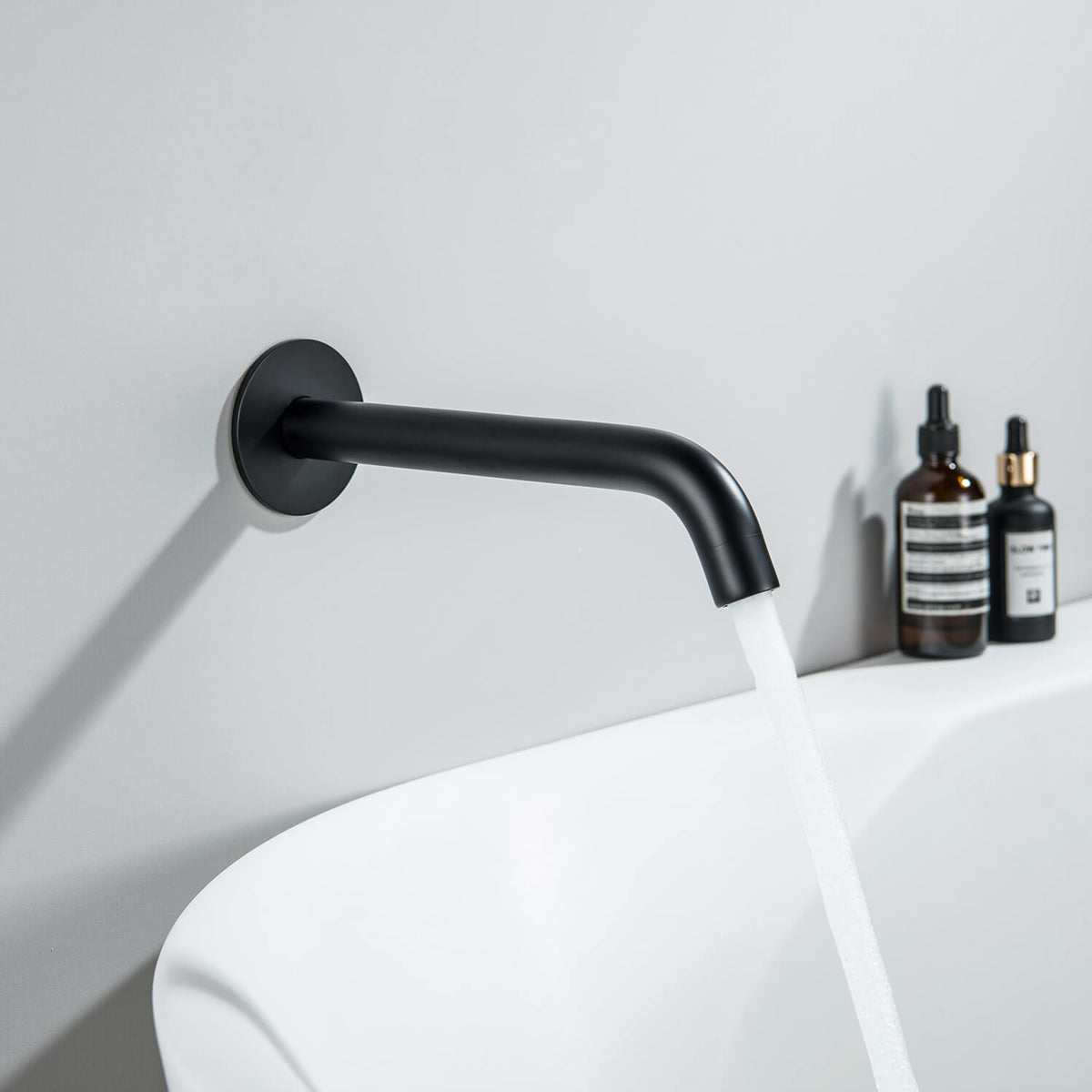 Aquavit Circular matte black wall-mounted bath spout installed above a bathtub